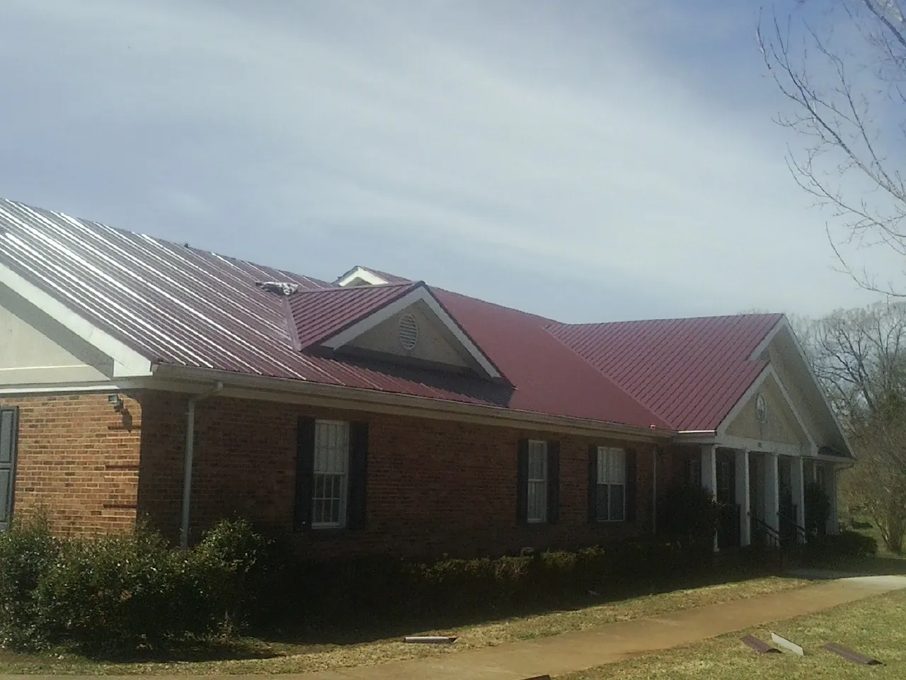 Red metal roof with gabled entries on a long brick building, from a Hail Damage Roof Repair job in San Quentin
