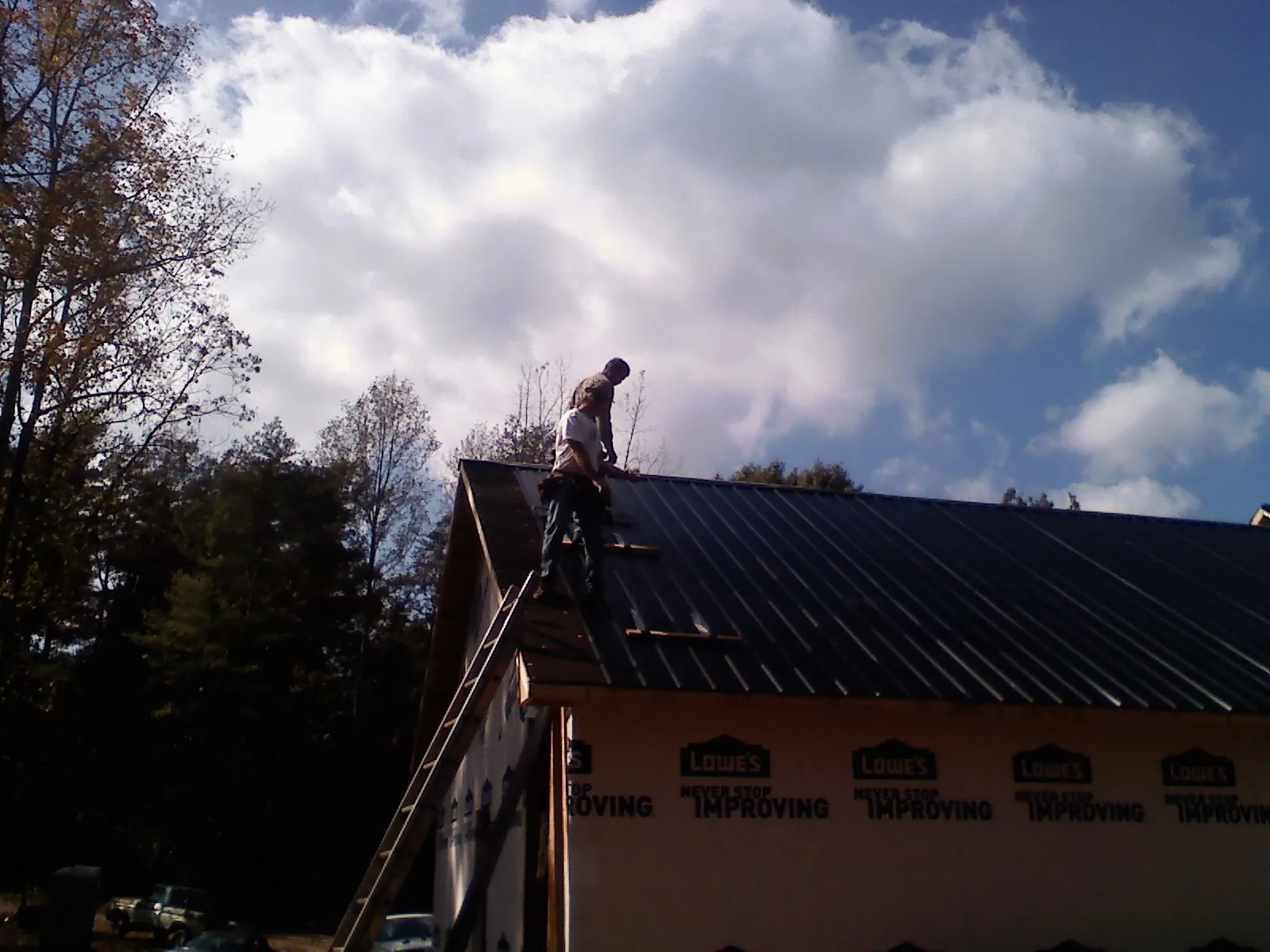 Roofer fastening dark metal panels high against a cloudy sky, from a Roof Inspection job in San Quentin