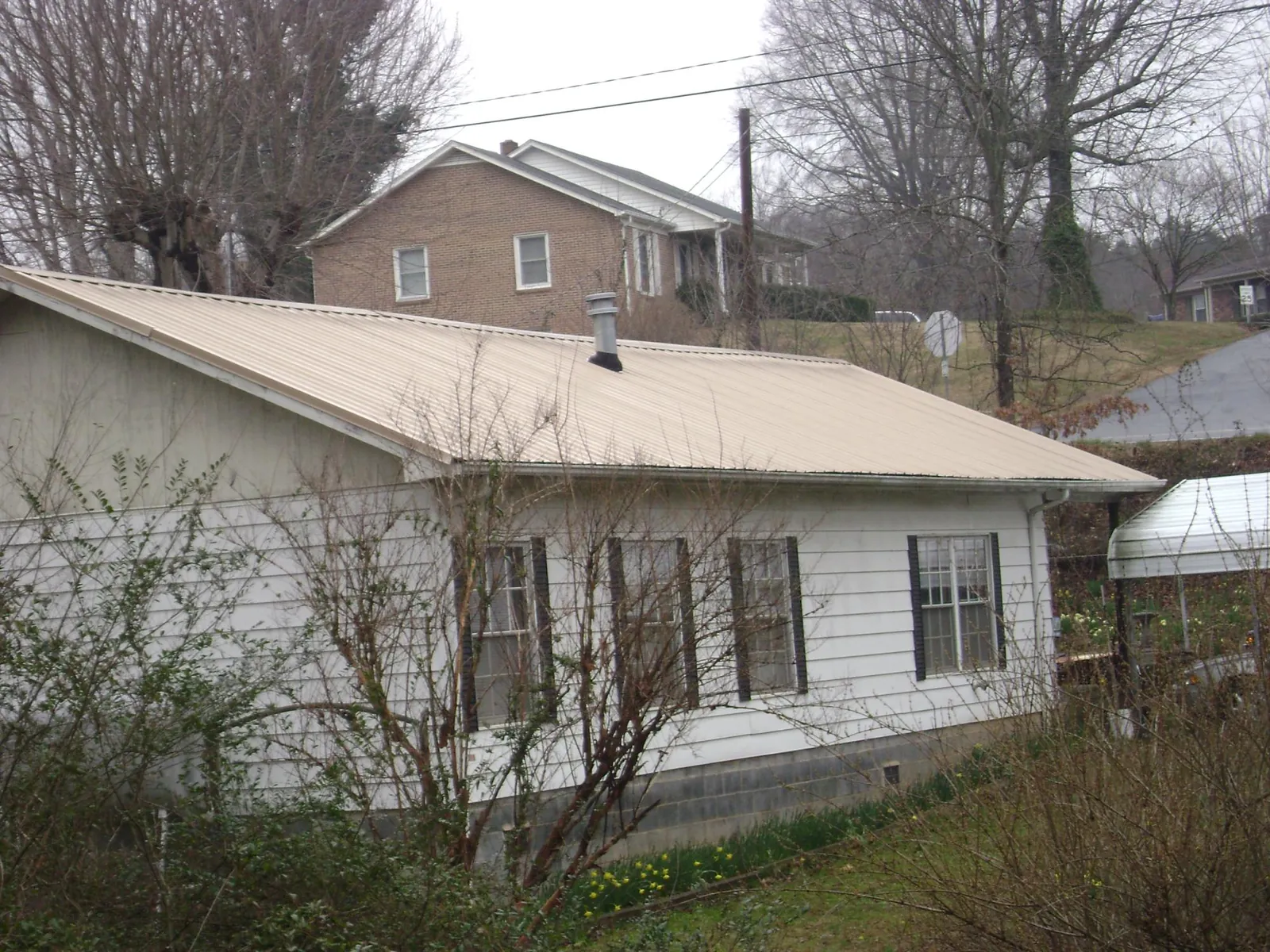 Tan metal roof on a white sided house set into a hillside — Commercial Roofing by Roofing Brothers in San Quentin